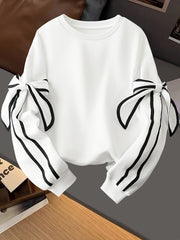 A white long-sleeve sweatshirt featuring decorative black-trimmed bows on the sleeves.
