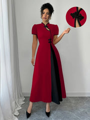A woman wears a fitted red midi dress with a black V-neck trim and decorative black buttons.