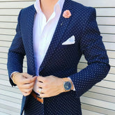 A man wears a dark blue slim-fit suit with a white polka dot pattern and a peaked lapel.