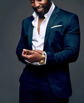 A man wearing a dark green two-piece suit with a white dress shirt and a gold watch.