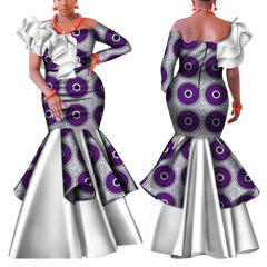 A woman models a purple and white patterned one-shoulder mermaid dress with a ruffled neckline.