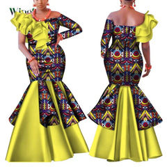 A woman models a long, one-shoulder African print dress with a yellow ruffled neckline and skirt.