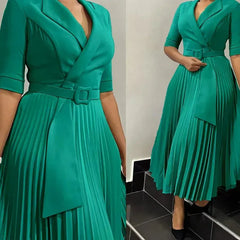 A woman wears a green, half-sleeve, V-neck pleated midi dress with a matching buckled belt.