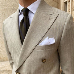 A slim-fit, double-breasted beige suit with subtle stripes, a peak lapel, and a white pocket square.