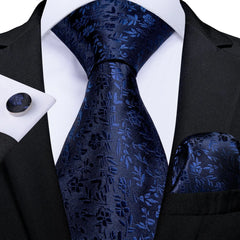 A navy blue silk necktie set featuring a floral pattern with a matching pocket square and cufflinks.