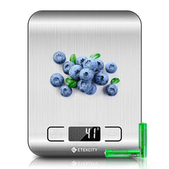 A stainless steel digital kitchen scale with a pile of blueberries and two batteries.