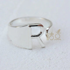 A silver-plated open ring featuring a prominent letter R design on a white background.
