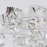 A collection of silver-plated open rings featuring various uppercase letter designs.
