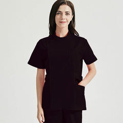 A woman wears a black short-sleeved medical scrub top with a side-button closure and pockets.