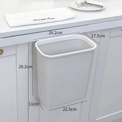 A light gray, rectangular, wall-mounted plastic trash can hangs on a white cabinet door.