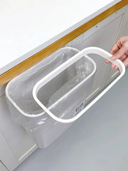 A white plastic hanging trash can mounted on a cabinet door with a removable top frame.