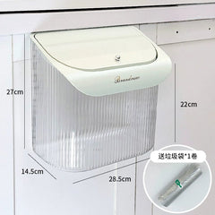 A wall-mounted, clear plastic kitchen trash can with a light-colored lid and a roll of trash bags.