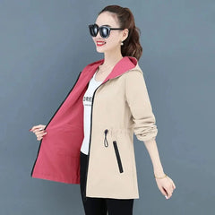 A woman wears a beige hooded windbreaker with a contrasting pink interior lining and zipper pockets.