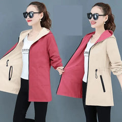A woman models a reversible hooded trench coat in red and beige with a zipper closure and pockets.