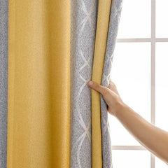 A hand holds a modern yellow and gray striped blackout curtain with a textured geometric pattern.