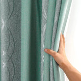 A hand holds a modern green and gray striped blackout curtain with a textured fabric finish.
