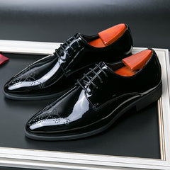 A pair of black glossy lace-up dress shoes with a pointed toe and decorative brogue detailing.