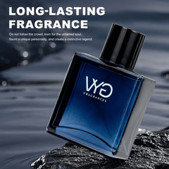 A square blue glass bottle of Charm Ocean Eau de Cologne sits on a dark rock near water.