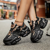 Women's black and metallic gold chunky lace-up sneakers with letter patch detailing.
