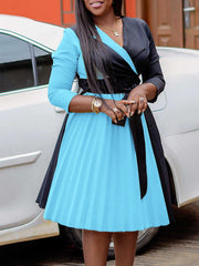 A woman wears a color-blocked V-neck dress with a black bodice and a pleated light blue skirt.