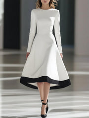 A woman wears a white long-sleeve midi dress with a black hem and a cinched waist.