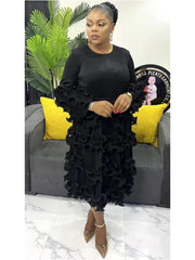 A woman wears a black mid-calf pleated dress with long sleeves and ruffled detailing.