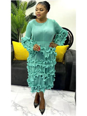 A woman wears a long-sleeved, mid-calf pleated mint green dress with ruffled detailing.
