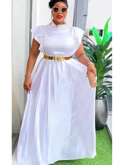 A woman wears a white sleeveless maxi dress with a high embellished neckline and a gold belt.