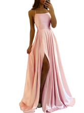 A woman wears a floor-length pink satin A-line gown with spaghetti straps and a high leg slit.