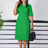 A woman wears a solid green, V-neck, short-sleeved midi dress with a matching waist belt.