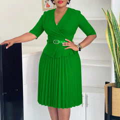 A woman wears a solid green V-neck midi dress with half sleeves, a belted waist, and a pleated skirt.