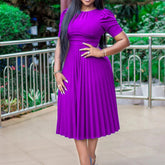 A woman wears a solid purple, short-sleeved, mid-calf length pleated midi dress.