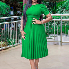 A woman wears a solid green, short-sleeved midi dress with a pleated skirt and an empire waist.