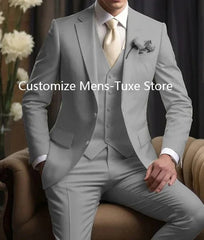 A man wears a light gray three-piece slim-fit suit with a matching vest and a cream-colored tie.