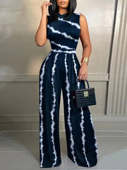 A woman wears a sleeveless, wide-leg jumpsuit featuring a dark blue and white tie-dye print.