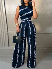 A woman wears a sleeveless, wide-leg jumpsuit featuring a dark blue and white tie-dye print.