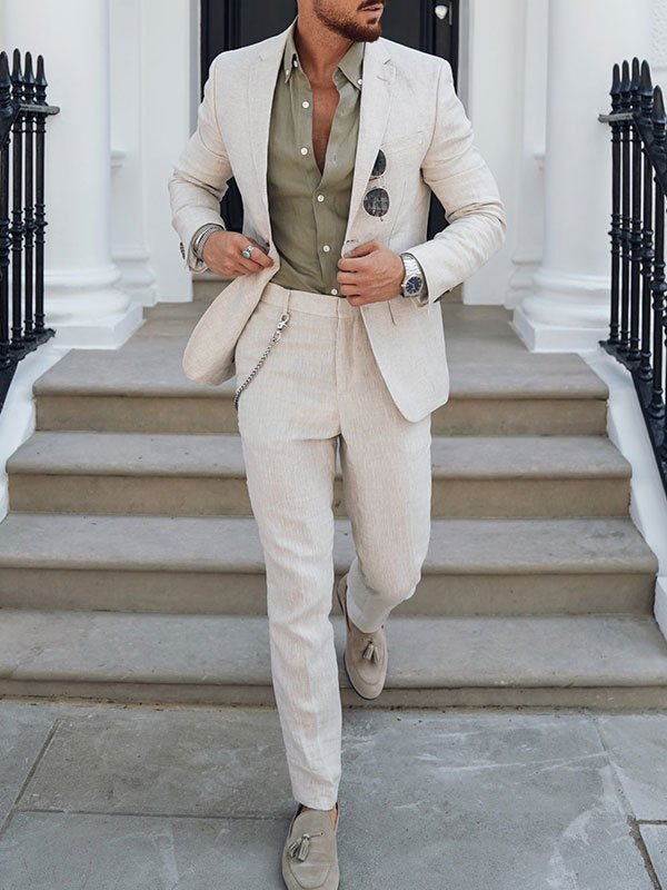 A man wears a slim-fit beige suit with an olive green button-down shirt and suede loafers.