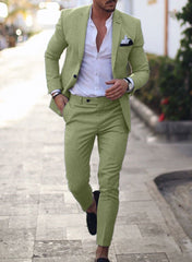 A man wears a slim-fit light green suit with a white button-down shirt and black loafers.