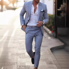 A man wears a slim-fit light blue suit with a white button-down shirt and dark loafers.