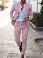 A man wears a slim-fit, light pink single-breasted suit with a white shirt and black loafers.