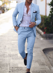 A man wears a light blue slim-fit suit with a white button-down shirt and black loafers.