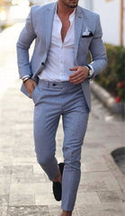 A man wears a slim-fit light blue suit with a white button-down shirt and black loafers.