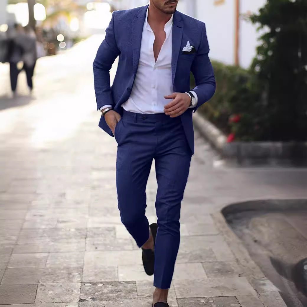 A man wears a slim-fit blue suit with a white button-down shirt and a pocket square.