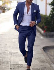 A man wears a slim-fit blue suit with a white button-down shirt and a pocket square.