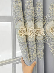 A hand holds a grey double-layer curtain featuring intricate cream-colored floral embroidery.