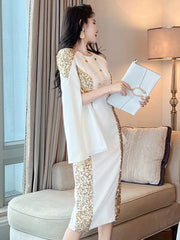 A woman wears a white knee-length pencil dress with gold sequin panels and cloak sleeves.