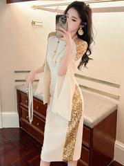 A woman wears a white knee-length pencil dress with gold sequin panels and cloak sleeves.