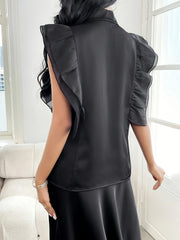A woman wears a black sleeveless blouse with a stand collar and ruffled shoulder details.