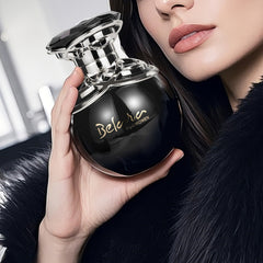 A woman holds a round, black Belara perfume bottle with a silver cap and gold lettering.