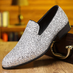 A silver glitter slip-on dress shoe with a pointed toe resting on a wooden surface.